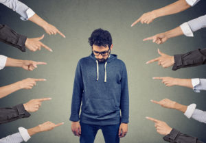 a man with his head bowed as fingers point at him