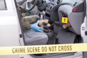 crime scene investigator pulling wrapped illegal drugs from car’s glove compartment