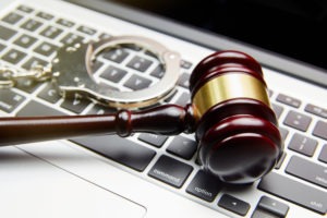 A gavel rests with handcuffs on top of a laptop keyboard. 