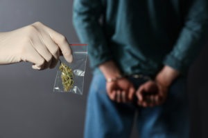 officer holds marijuana baggie behind handcuffed suspect