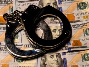 California PC §186.2 | Criminal Profiteering | Simmrin Law Group Handcuffs set on top of rows of $100 bills