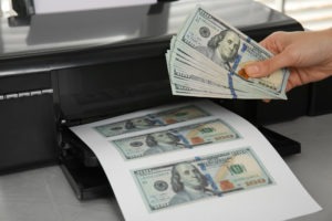 fake hundred-dollar bills on printer and hand fanning out counterfeit bills