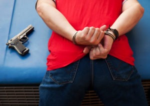 Felon in Possession of a Firearm Lawyer in Los Angeles | Free Consultations 24/7 suspect hunched over car in handcuffs with gun next to him