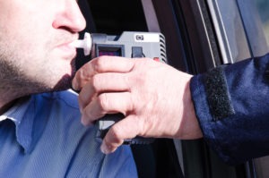 Probable Cause for DUI in a Parked Car | Simmrin Law Group officer holds breathalyzer for motorist sitting in driver’s seat