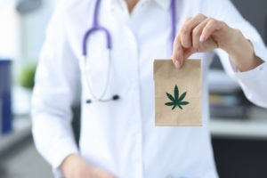 a doctor holding a small paper bag with a marijuana leaf picture on it