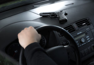 a gun sitting on the dashboard of a car with a hand on the steering wheel