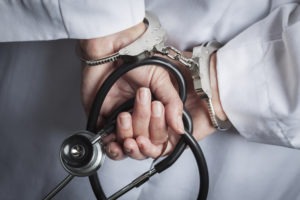 Health Care Fraud Attorney in Los Angeles | Simmrin Law Group doctor in handcuffs holding stethoscope