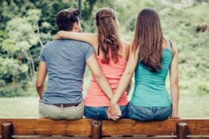 man hugs woman while holding second woman’s hand