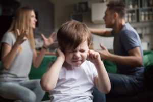 child plugging ears as parents fight
