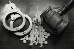 Image of drugs together with handcuffs and gavel.