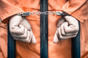 handcuffed-prisoner-hands-behind-bars
