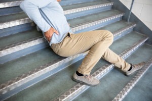 Slip and Fall Accident Lawyer in Fullerton | Free Consultations 24/7 A man in a blue dress shirt and khakis lies on a staircase after falling.