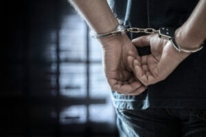 A man is handcuffed with his hands behind his back because in California, it is illegal to tell someone to commit suicide under Penal Code Section 401. If you were charged, a criminal defense lawyer can help you build a strong defense.