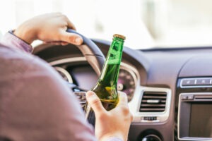 A driver holding a bottle of alcohol while in a car with a minor in the back seat. Discover if having a minor present with alcohol in the car is legal in California. 
