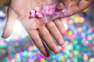 Closeup shot of a man pouring pink heart shaped pills on its palm from a transparent ziplock bag on bright blurry background. Is MDMA legal in the US?